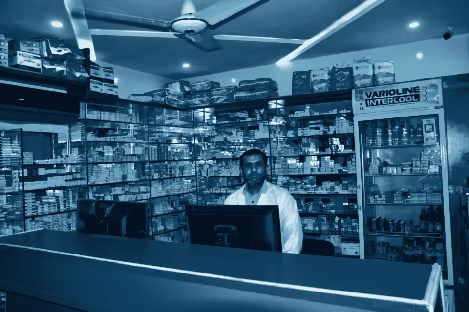 Pharmacist behind the counter of a hospital pharmacy lined with medicine shelves