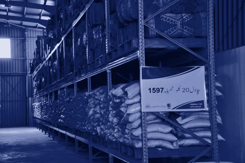 Racks of rice sacks in a warehouse with an Urdu price board
